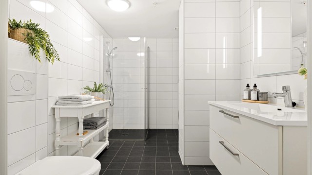 Tidløst og helfliset bad med varme i gulv. Badet er innredet med vegghengt toalett, dusj med glass foldedører, servant med møblement, speil og belysning.