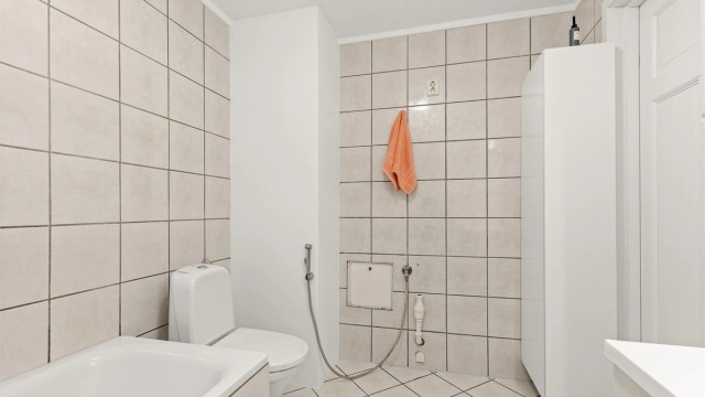 Gulvmontert toalett og flislagte gulv med elektrisk gulvvarme og flislagte vegger.