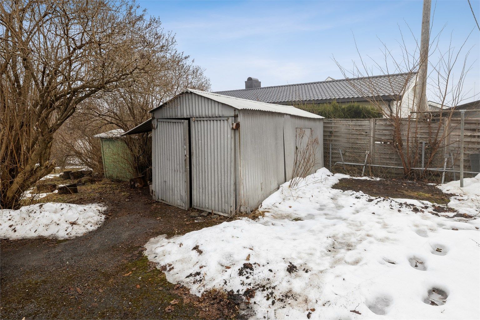 På tomten står en eldre, frittstående garasje og en bod.