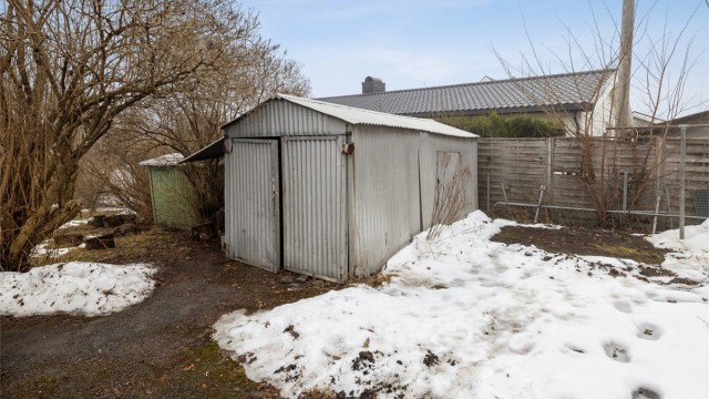 På tomten står en eldre, frittstående garasje og en bod.