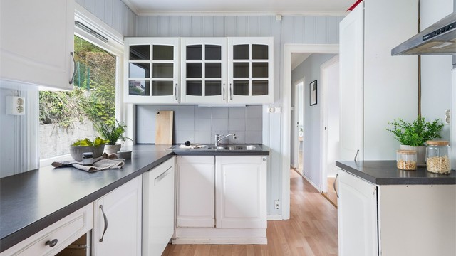 Kjøkkenet har fliser over benken, vegghengt ventilator og opplegg for oppvaskmaskin.