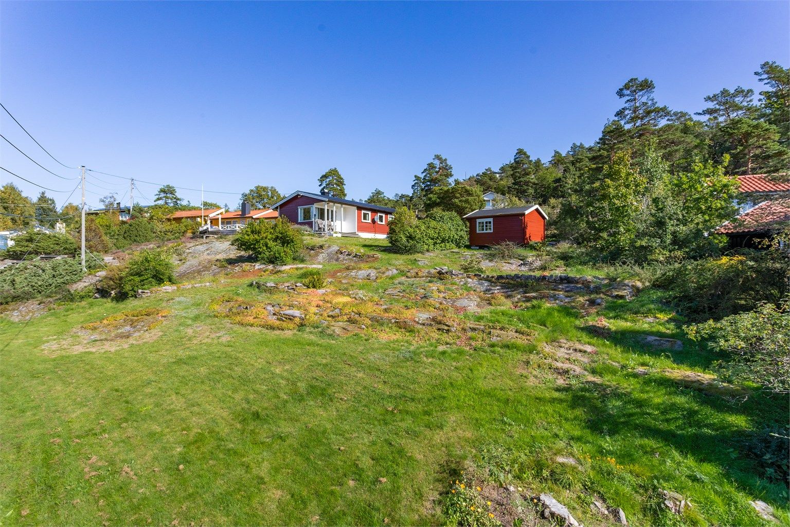  Eiendommen har naturlig uteareal med gress, berg, beplantning og trær. Det er også en praktisk redskapsbod i hagen. Her er det ordentlig sommeridyll!
