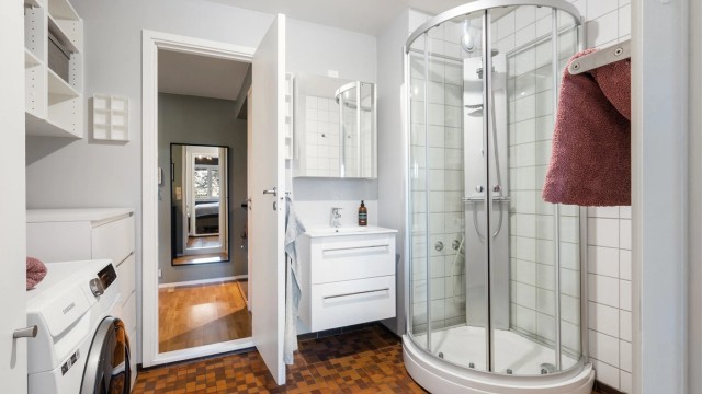 Baderommet har flislagt gulv med varmekabler, dusjkabinett og opplegg for vaskemaskin.