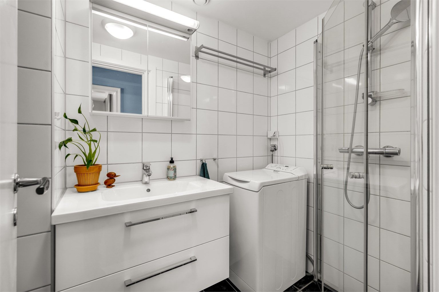 Pent, flislagt bad med varmekabler i gulvet. Badet er innredet med vegghengt servantinnredning med ovenpåliggende vask og speilskap med belysning over vasken.