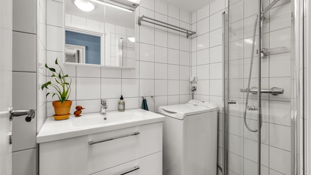 Pent, flislagt bad med varmekabler i gulvet. Badet er innredet med vegghengt servantinnredning med ovenpåliggende vask og speilskap med belysning over vasken.