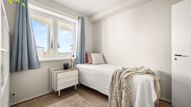 Rommet har plass til seng og oppbevaring, og de lyse overflatene kombinert med vindusflater gir en luftig og hyggelig atmosfære.