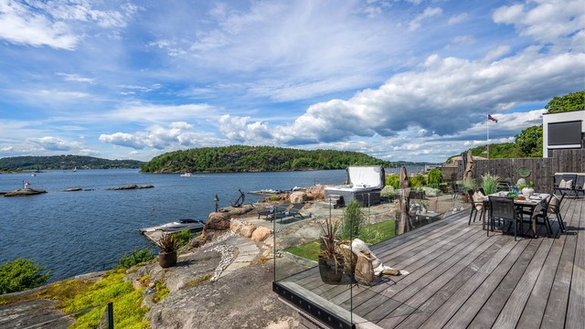 Utgang fra stue og spisestue i 1. etasje via store skyvedører til vestvendt terrasse oppført med vedlikeholdsvennlig tredekke og rekkverk i glass.