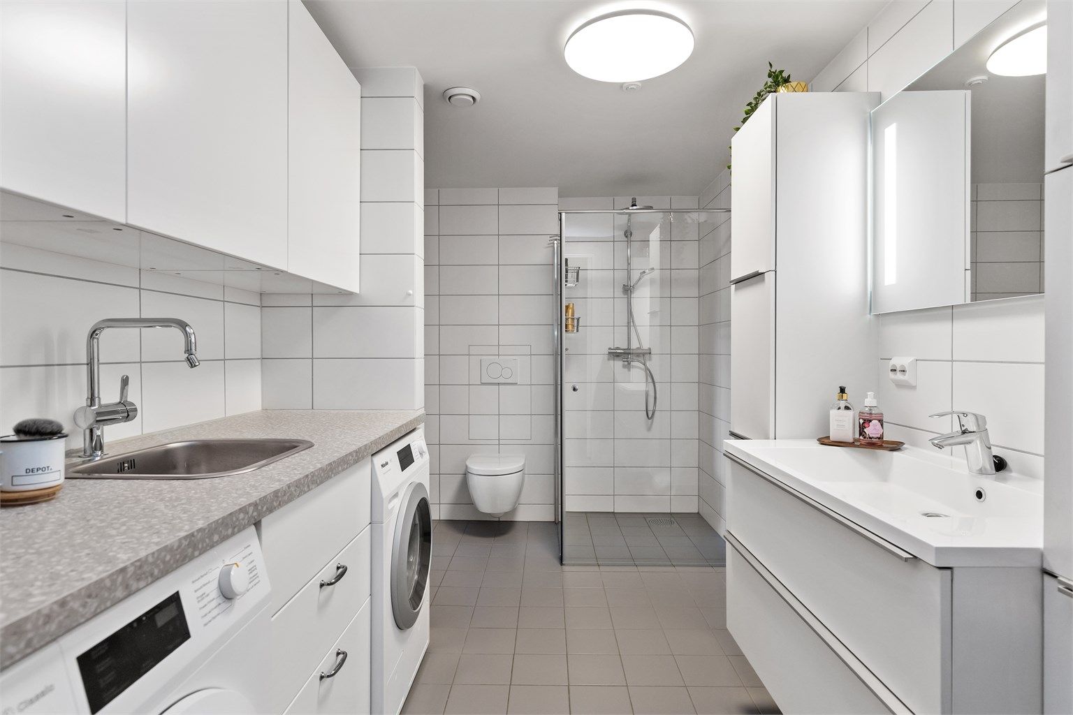 Stort, flislagt bad fra 2019 med gulvvarme, dusjnisje og en praktisk vaskeromsdel.