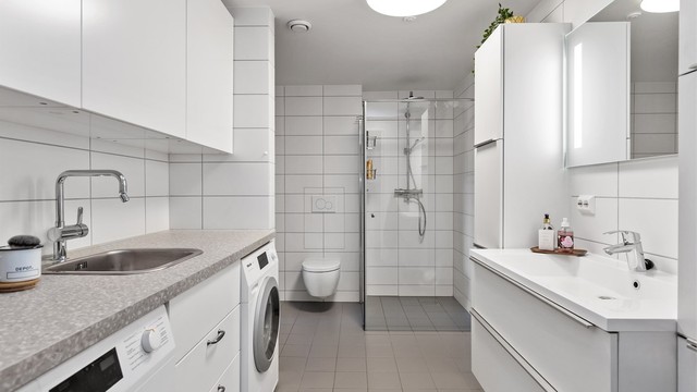 Stort, flislagt bad fra 2019 med gulvvarme, dusjnisje og en praktisk vaskeromsdel.