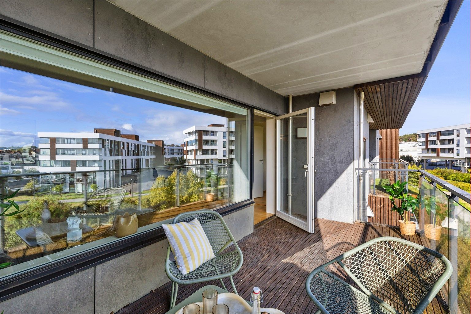 Overbygd balkong med dekke av terrassebord og rekkverk i metall og glass.