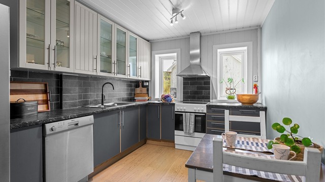 Fliser på vegg mellom benk og overskap. Stikkontakter over kjøkkenbenk. Plass for frittstående komfyr, kjøleskap og oppvaskmaskin.