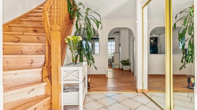 Romslig entré med skyvedørsgarderobe og trapp i lakkert tre som leder opp til andre etasje.