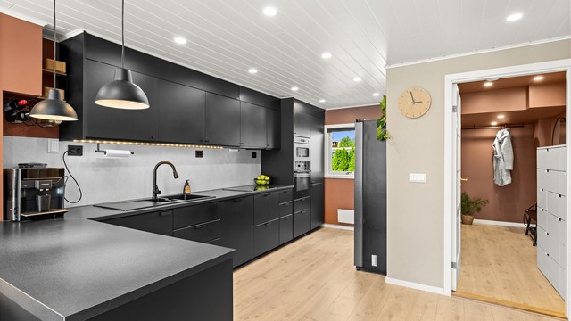 Kjøkkenet ligger i åpen løsning mot stuen med downlights i himling og lekker, stilren kjøkkeninnredning fra 2020.