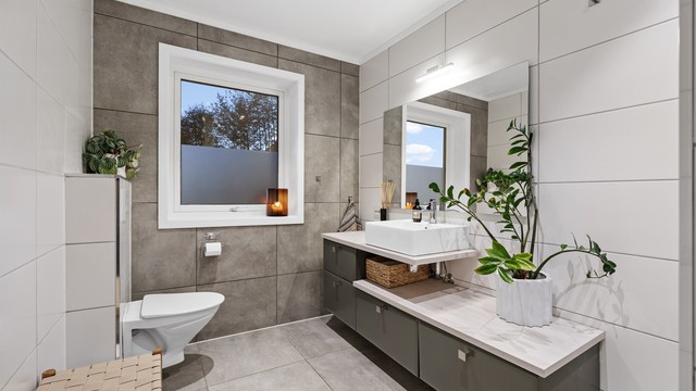 Badet har flislagte overflater, gulvvarme og baderomsinnredning med ovenpåliggende servant.