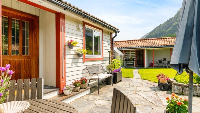 Pent inngangsparti med hellelagt uteplass og gangvei fra garasje og parkeringsplass.