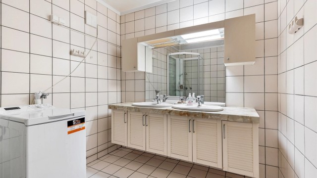 Baderom i kjelleretasjen er fra byggeår med flislagt gulv med varme og flislagte vegger. Badet har vegghengt servantinnredning, ovenpåliggende dobbeltservant med armaturer og vegghengt skap ved speil.