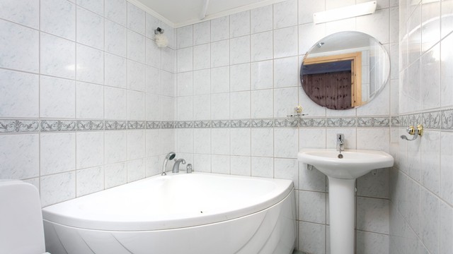 Kombinert bad og vaskerom i kjelleren med fliser, gulvvarme og hjørnebadekar.