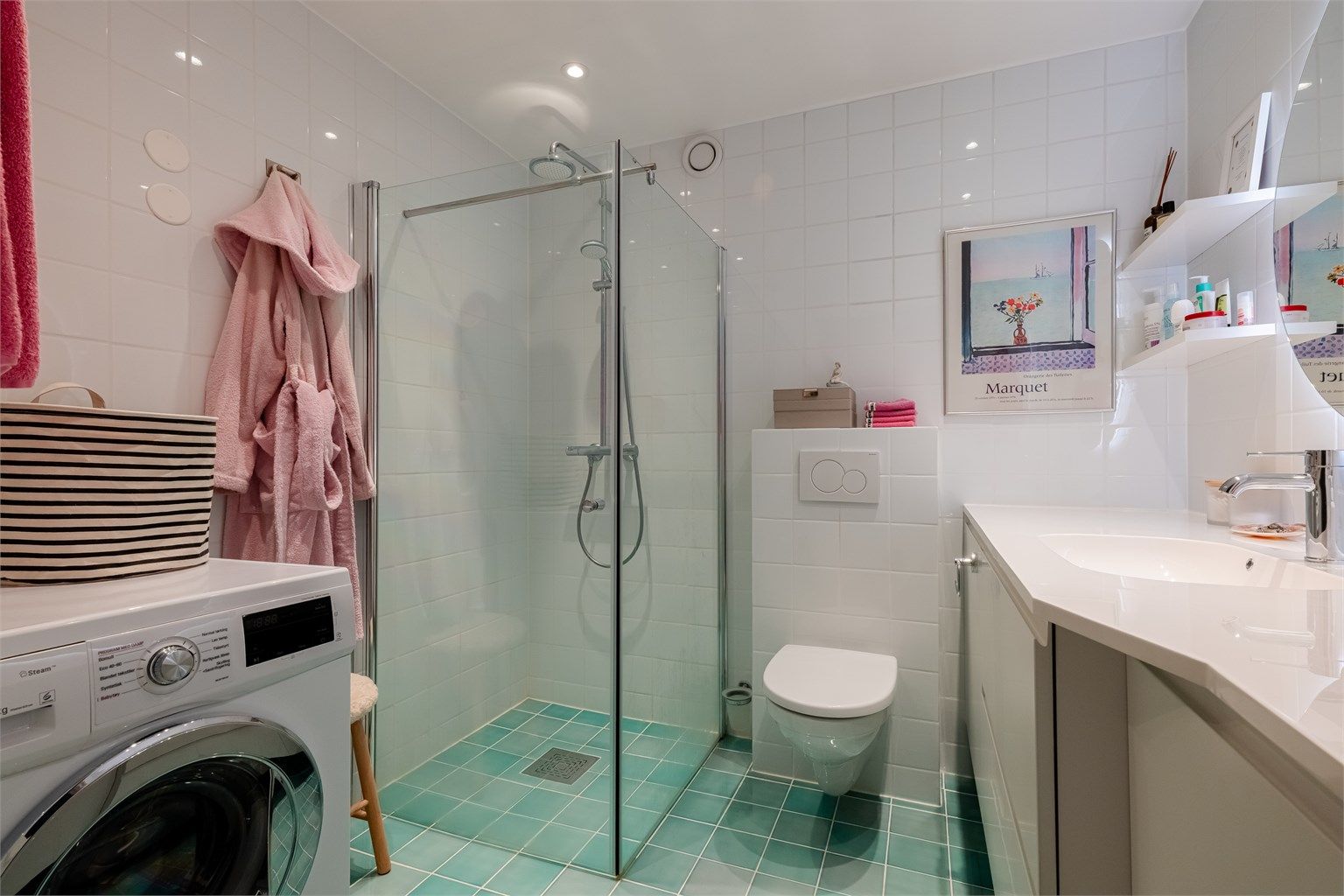 Badet er innredet med vegghengt toalett tilkoblet sisternekasse og egen dusjsone med glassfelt og glassdør. Dusjen er tilkoblet både hånd- og regndusj.
