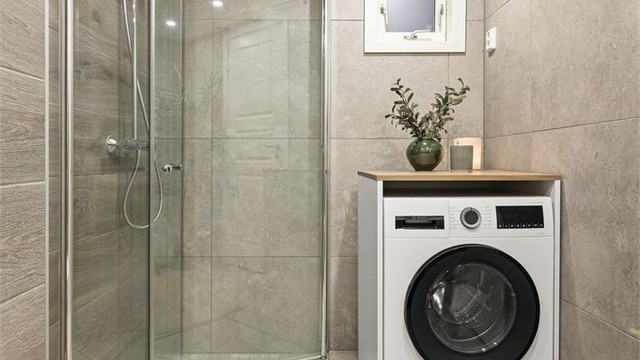 Videre er det dusjhjørne med glassdører i tillegg til opplegg for vaskemaskin.