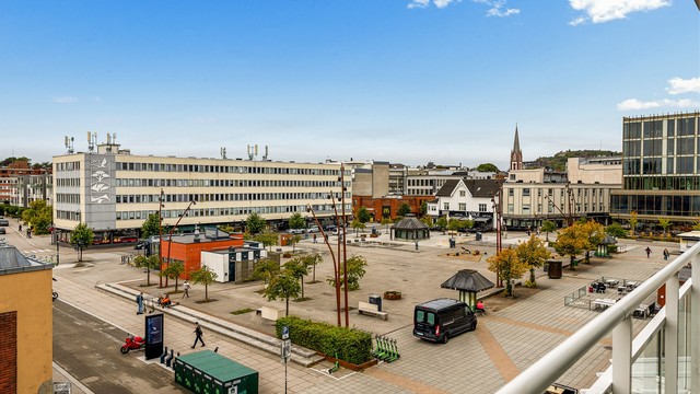 Åpent utsyn over Torget med byliv og kirketårnet i bakgrunnen.