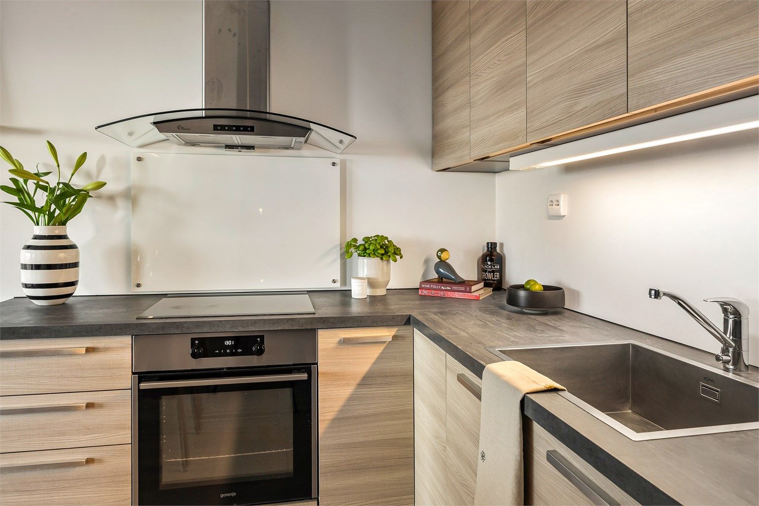 Glassplate på vegg ved stekeområde. Laminert benkeplate. Lysarmatur under overskap.