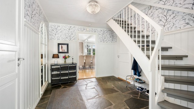 Lys hall med bruddskifer på gulvet, trapp til loftsetasjen og dør inn til stuen.