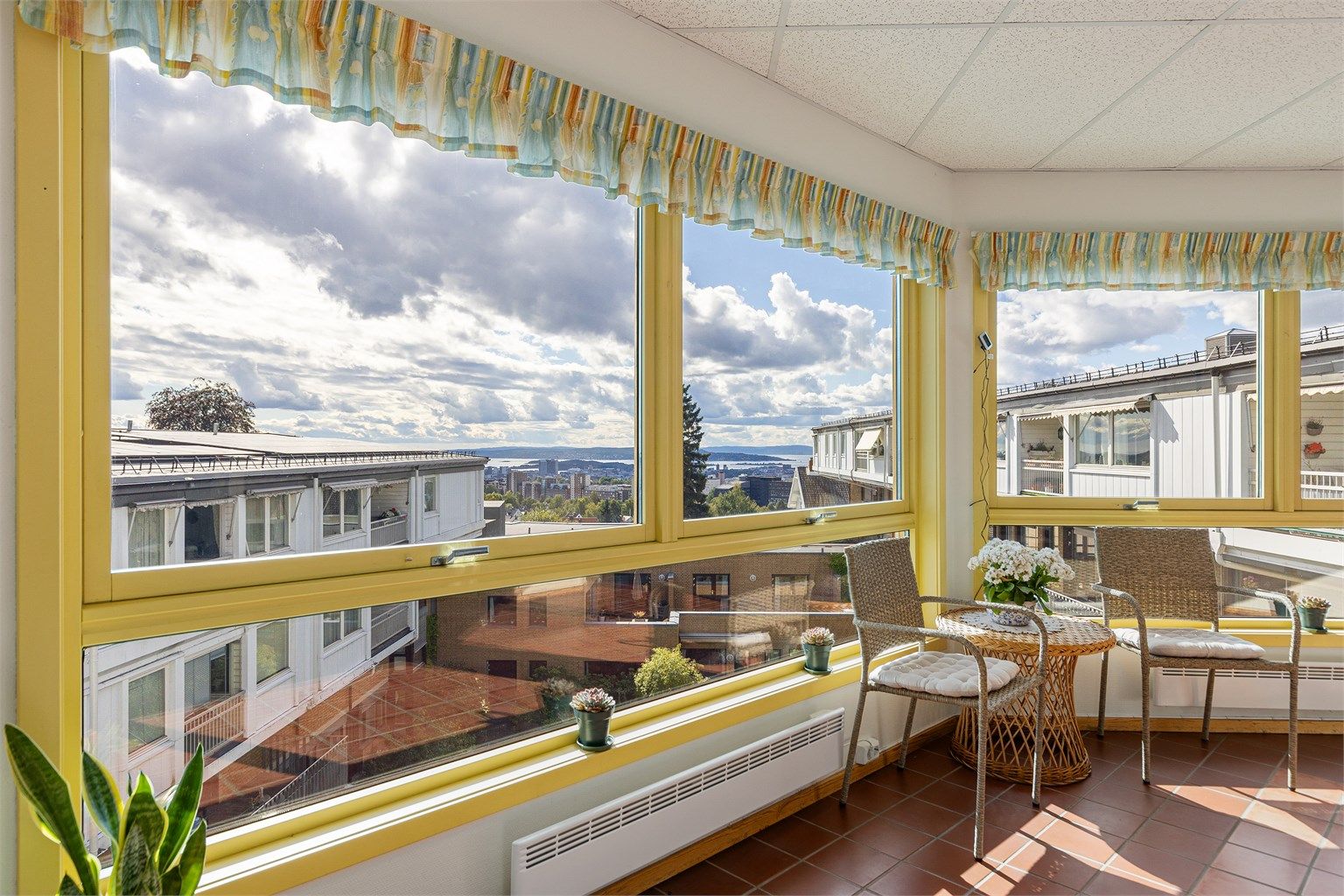 Felles innglasset oppholdsareal med sitteplasser og flott fjordutsikt.