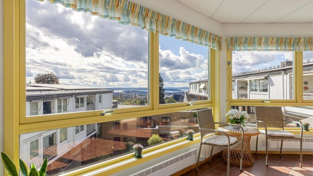 Felles innglasset oppholdsareal med sitteplasser og flott fjordutsikt.
