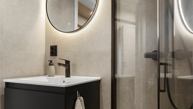 Badet har baderomsinnredning, speil med integrert belysning, dusjhjørne med regnfallsdusj og vegghengt toalett.