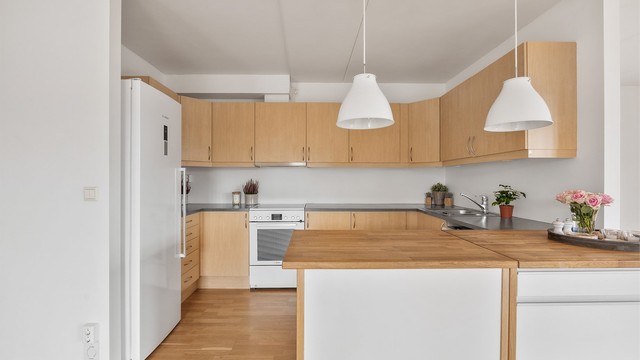 Kjøkken med glatte fronter og kjøkkenøy med benkeplate av tre.