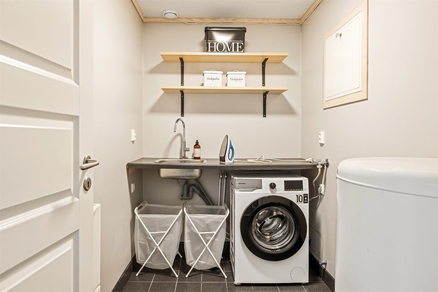 Praktisk vaskerom med flislagt gulv med varmekabler, opplegg for vaskemaskin og utslagsvask.