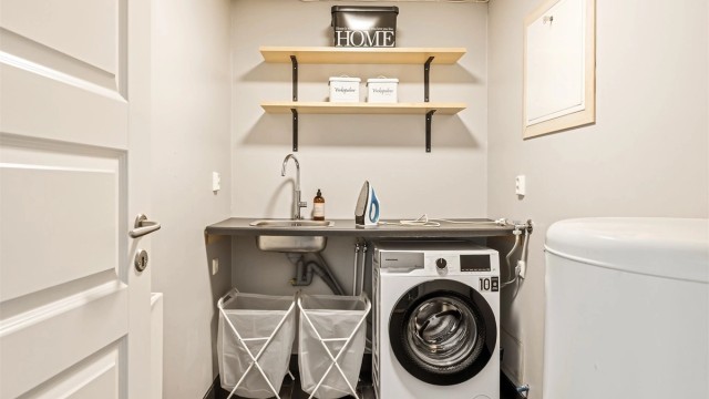 Praktisk vaskerom med flislagt gulv med varmekabler, opplegg for vaskemaskin og utslagsvask.