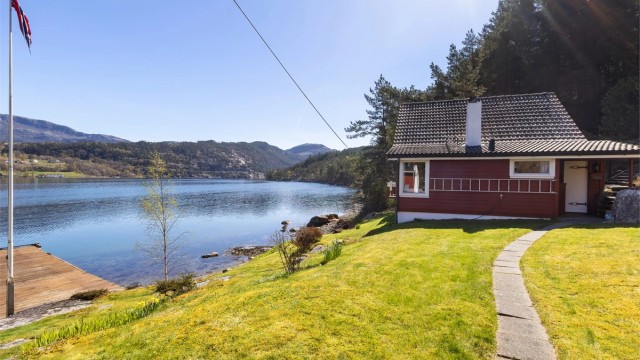 En velholdt gressplen omkranser hytta og bryggeområdet.