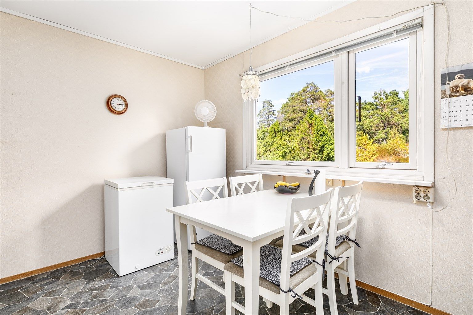 Foran kjøkkenvinduene er det plass til et spisebord og hverdagens måltider. På denne siden titter morgensolen inn sommerstid.