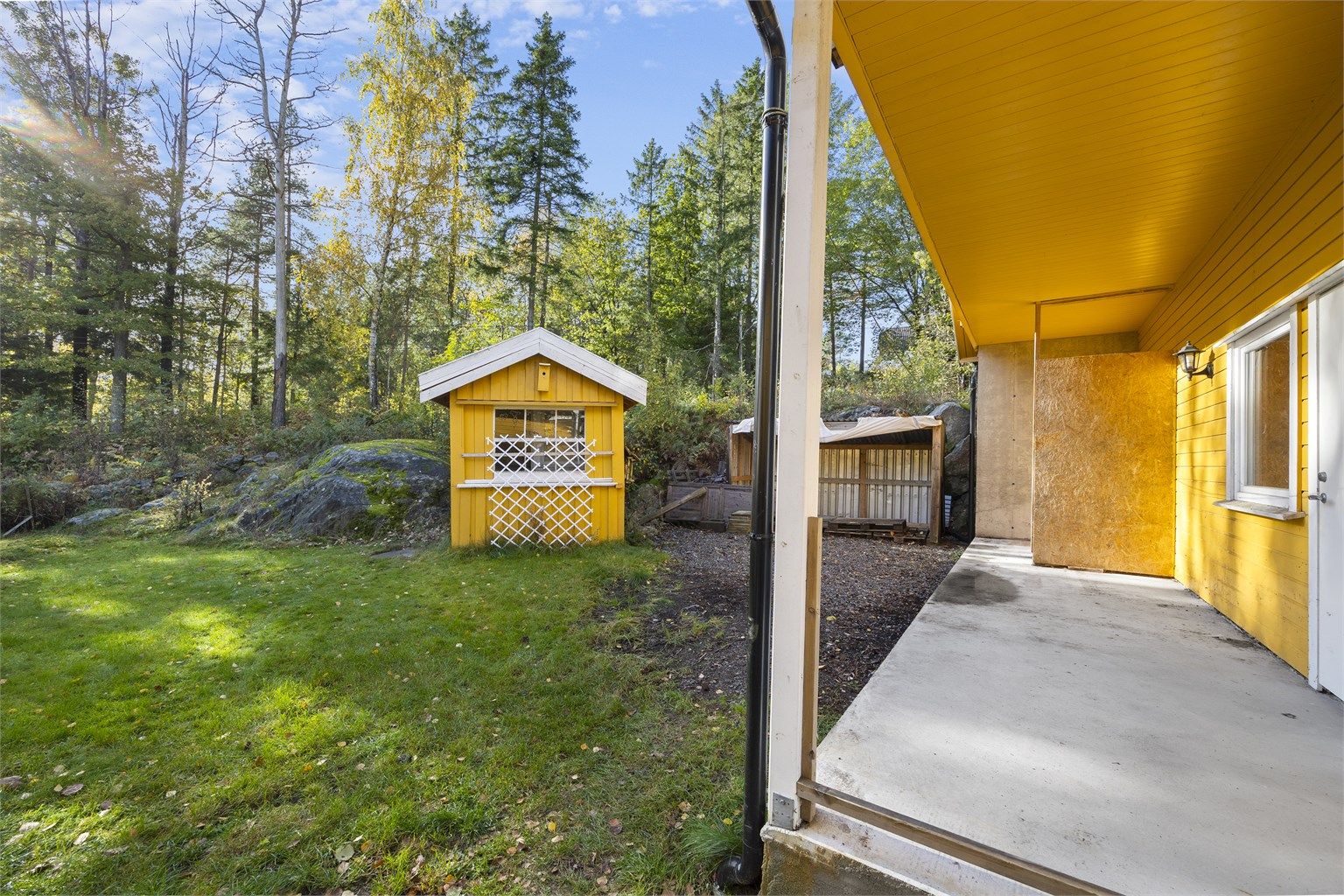 Skjermet uteområde på bakkeplan med utsikt mot den grønne hagen og redskapsbod.