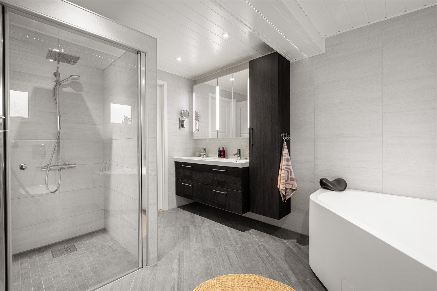 De mørke baderomsmøblene gir en fin kontrast til de lyse flisene. Med dobbelt servantoppsett og rikelig med oppbevaringsplass, er dette et baderom som dekker hele familiens behov.