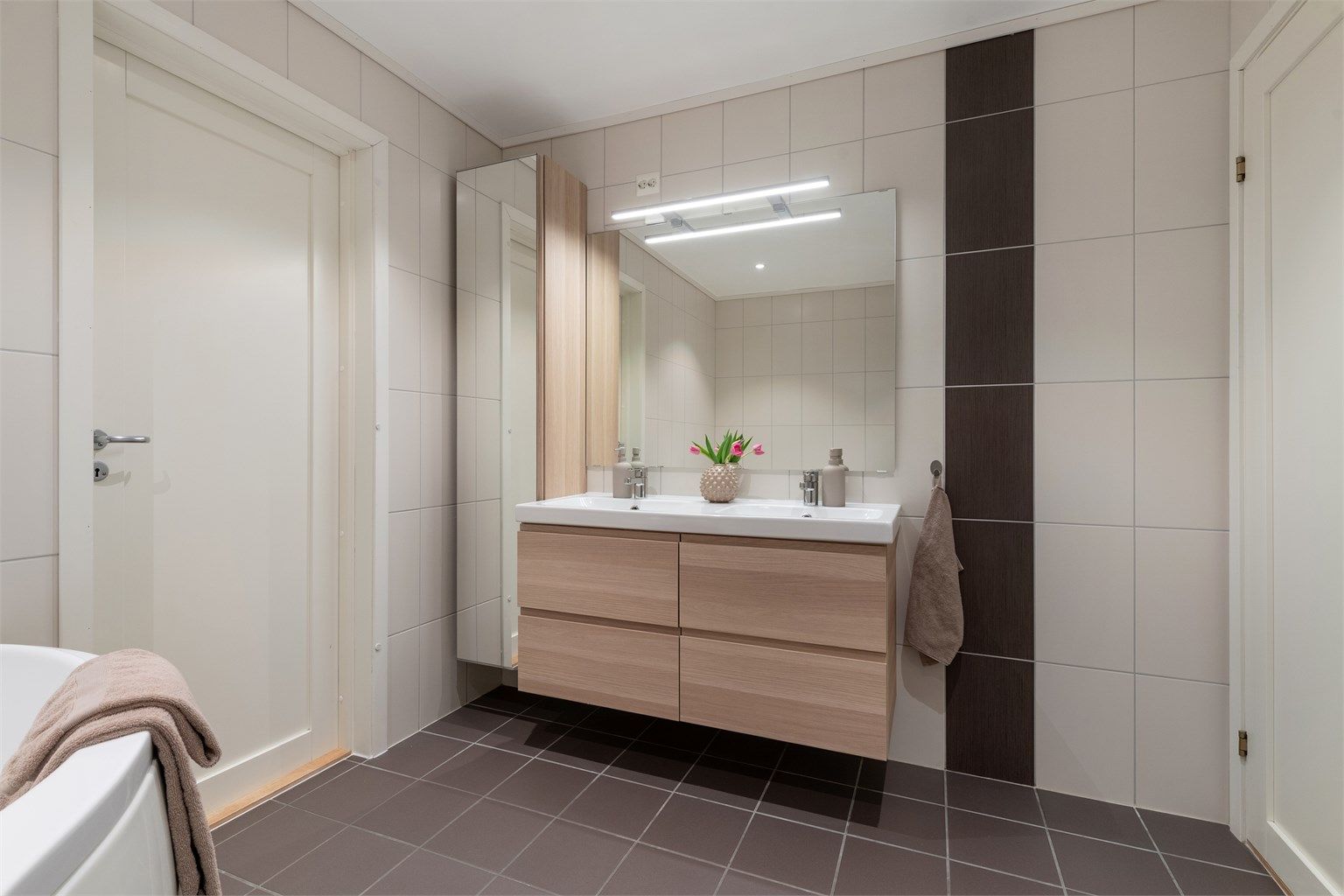 Badet har en dobbel, ovenpåliggende servant med vegghengt innredning og høyskap for ekstra oppbevaring.