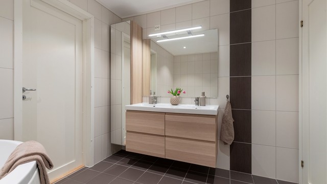 Badet har en dobbel, ovenpåliggende servant med vegghengt innredning og høyskap for ekstra oppbevaring.