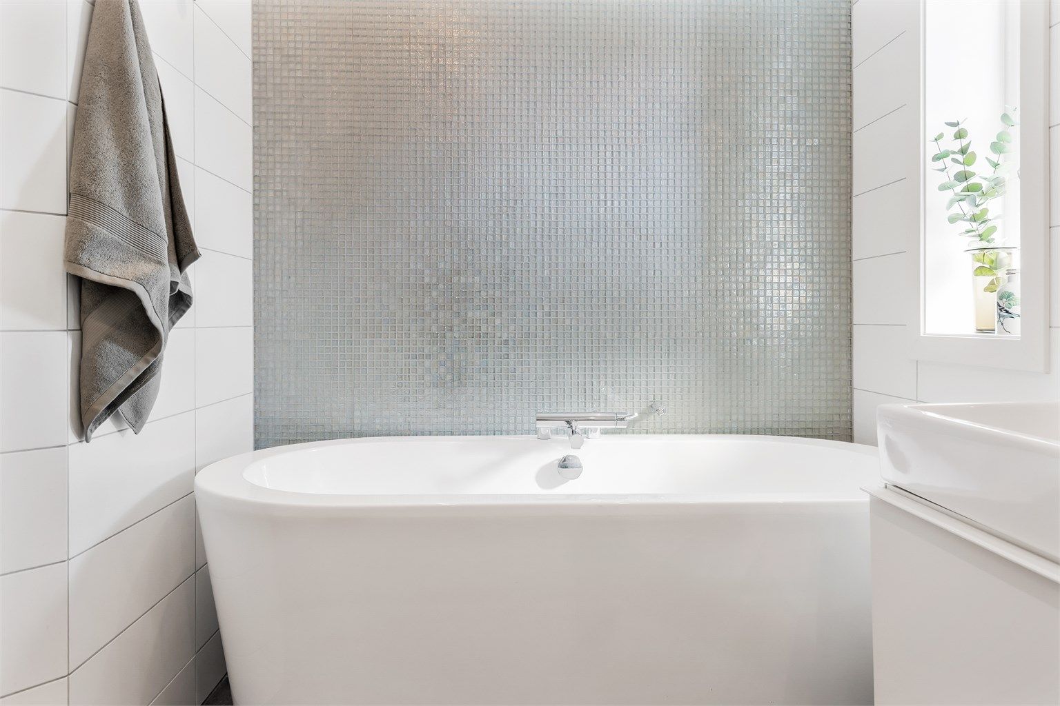 Frittstående badekar med dusjarmatur. Mekanisk avtrekksventil i himling. Glassfliser fra Fired Earth.