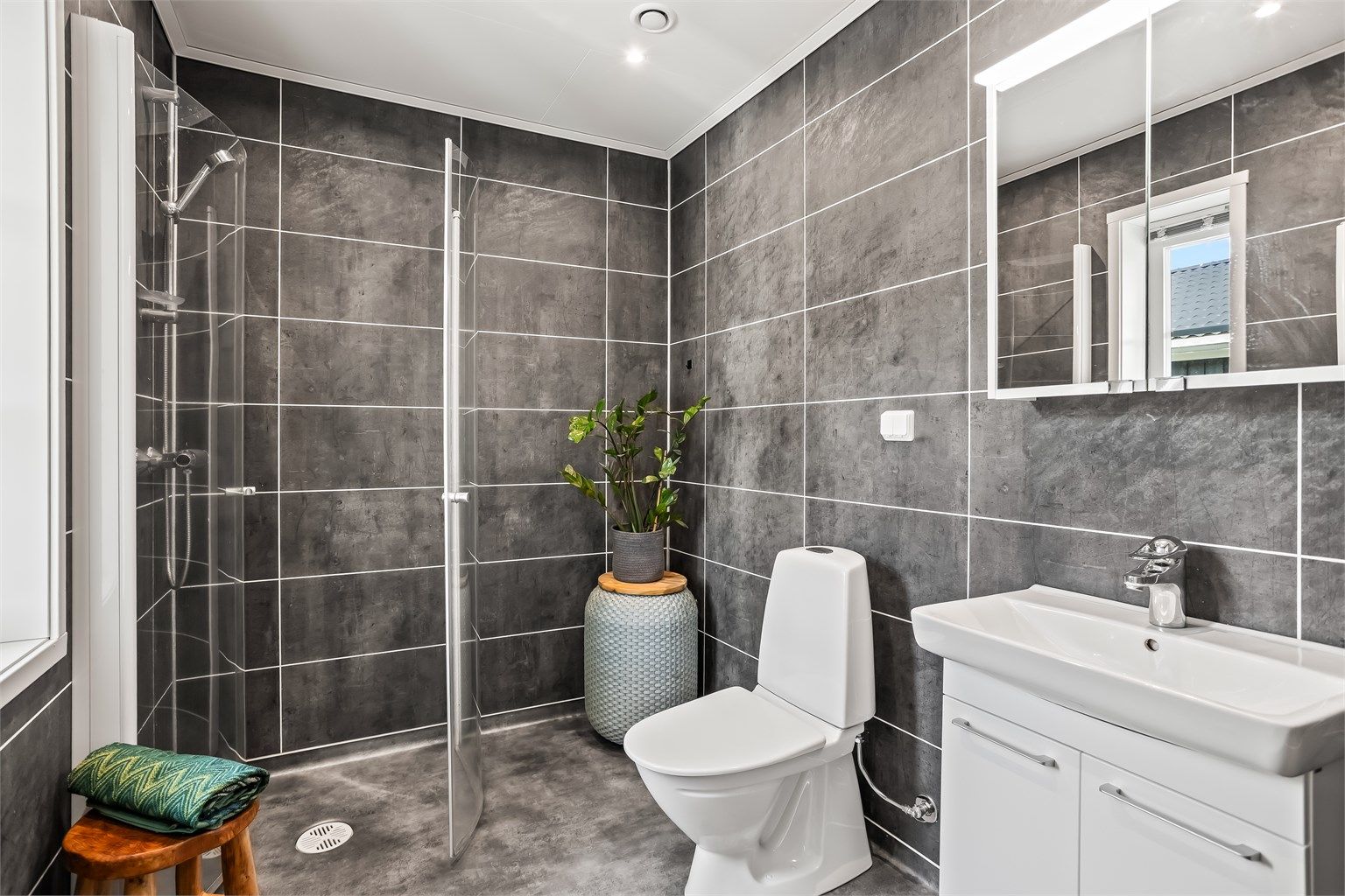 Fra entréen har du tilgang til boligens første bad. Badet er utstyrt med toalett, dusj og servant med skap.