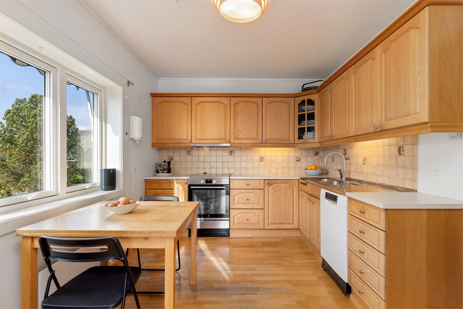 Kjøkkeninnredning med profilerte trefronter, fliser over benk og laminert benkeplate.