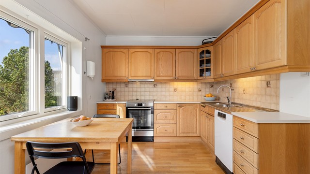 Kjøkkeninnredning med profilerte trefronter, fliser over benk og laminert benkeplate.