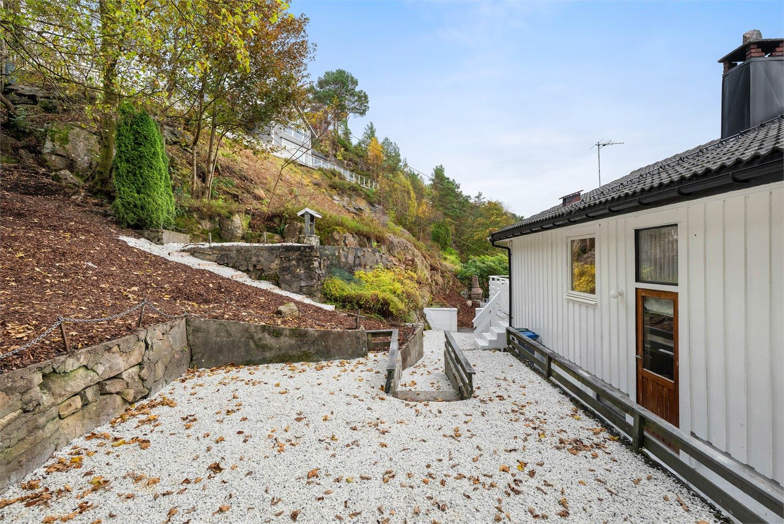 Baksiden er pent opparbeidet med singel, trapper og forstøtningsmurer.