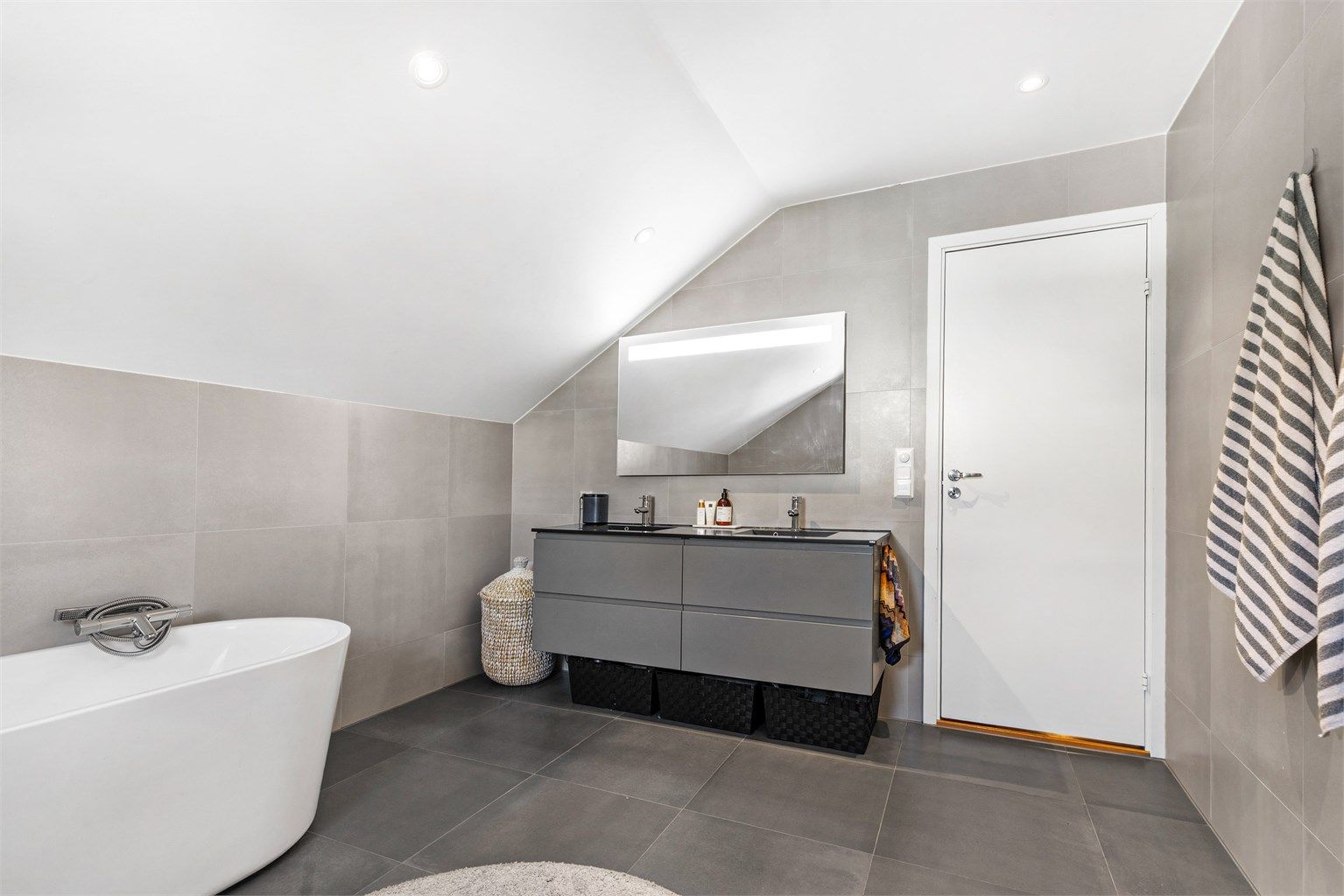 Speil med overlys og stikkontakt over servant. Badekar med vegghengt badekararmatur. Vegghengt toalett.