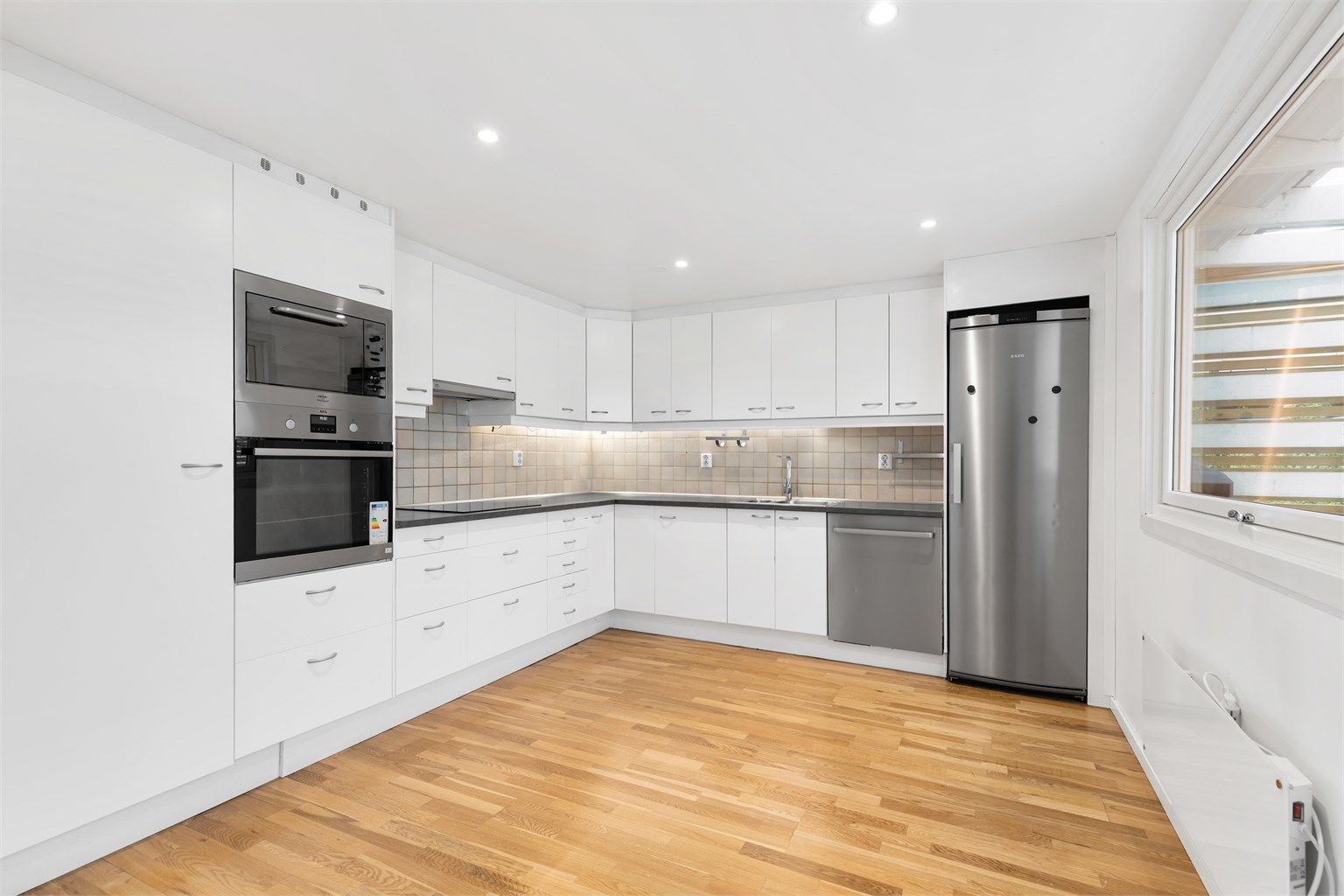 Lyst og moderne kjøkken med plass til kjøkkenøy eller spisebord.