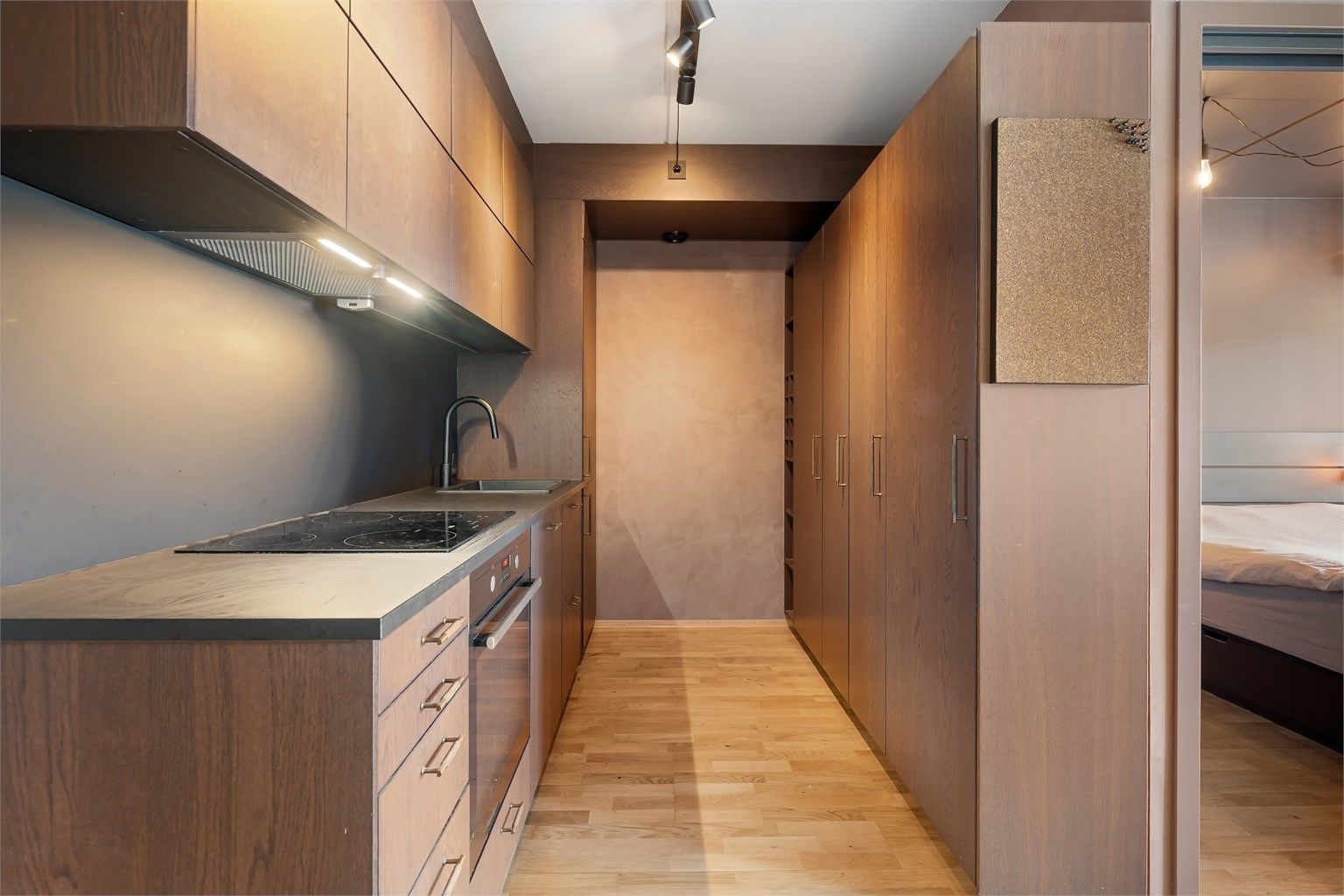 Lekkert og moderne kjøkken fra 2021 med mørke fronter, rustikk veggplate mellom kjøkkenbenk og overskap og integrerte hvitevarer som komfyr, induksjonstopp, oppvaskmaskin og kjøleskap med fryser