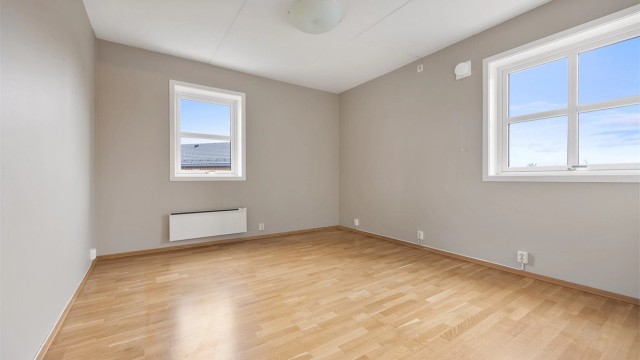Hovedsoverom med vinduer på to vegger og god plass til dobbeltseng.