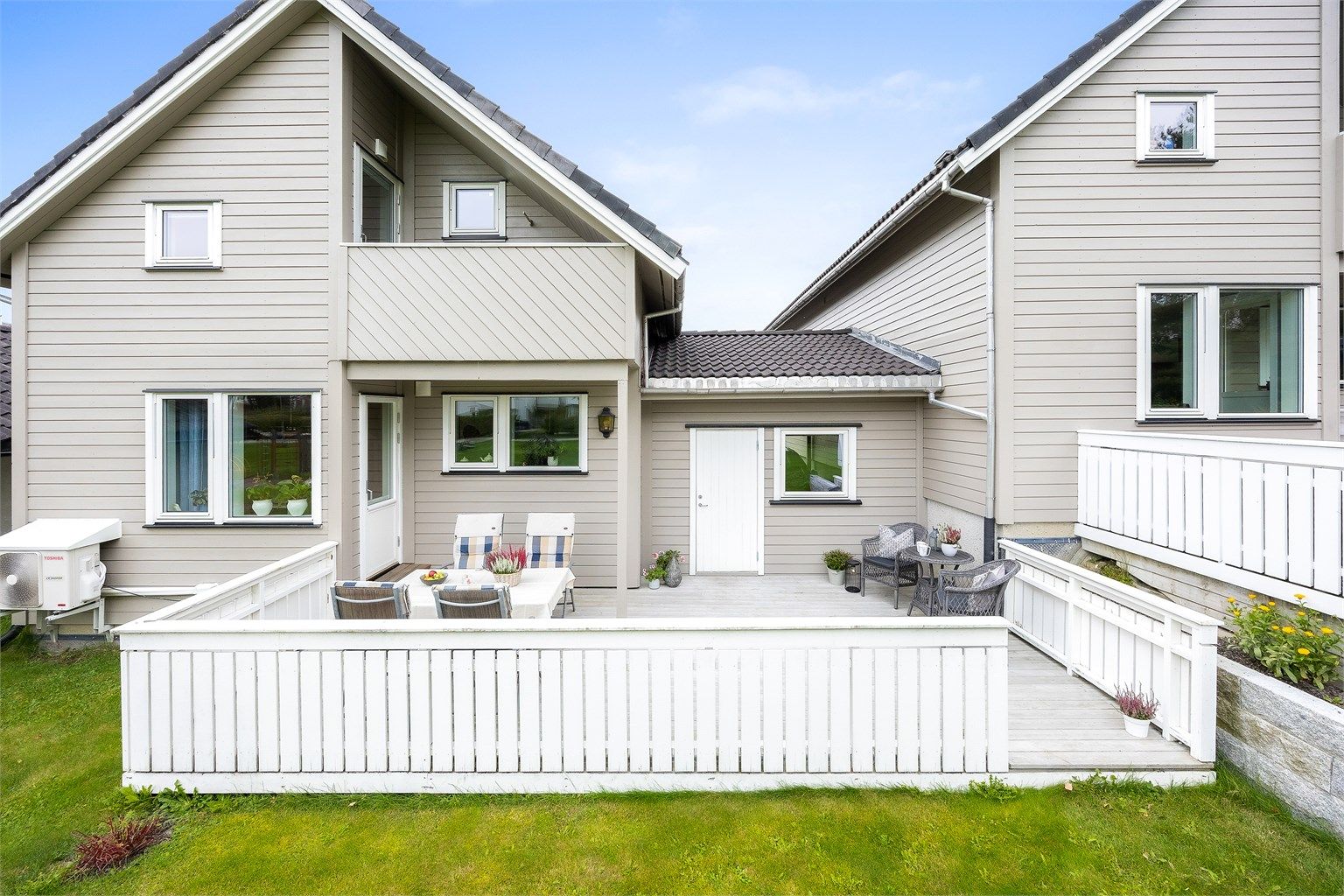 Fasaden mot hagen med terrasse på bakkeplan og overbygd veranda i loftsetasjen.