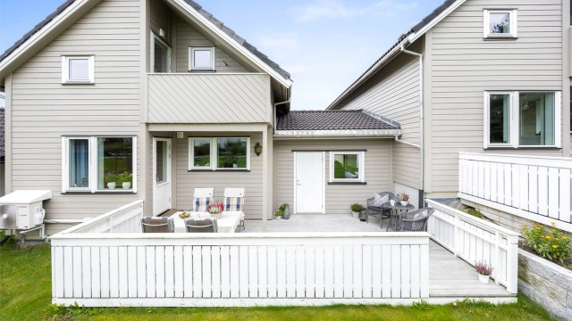 Fasaden mot hagen med terrasse på bakkeplan og overbygd veranda i loftsetasjen.