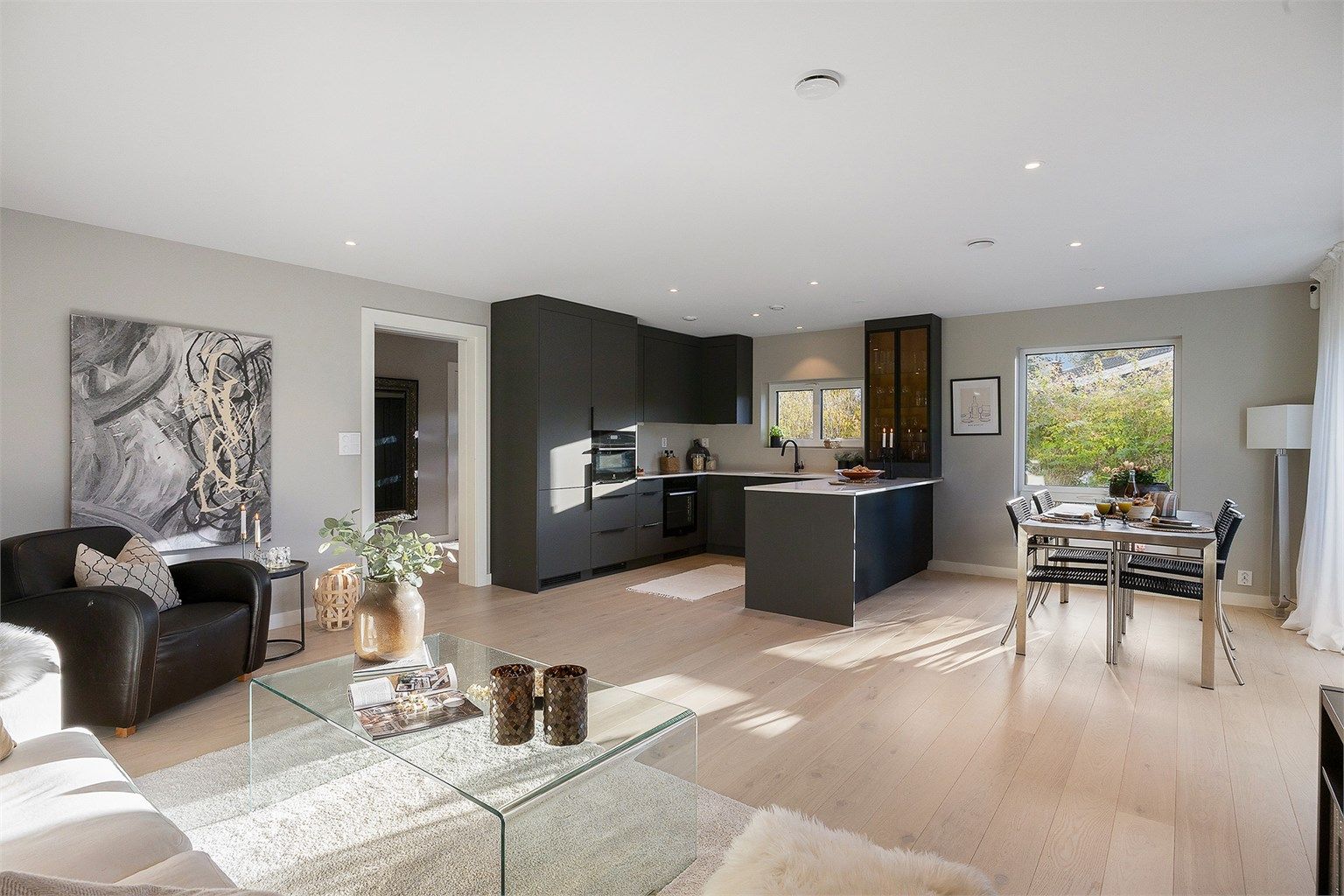 Praktisk åpen løsning mellom stue og kjøkken, med lyse vegger og lys eikeparkett som gir en lys og luftig atmosfære